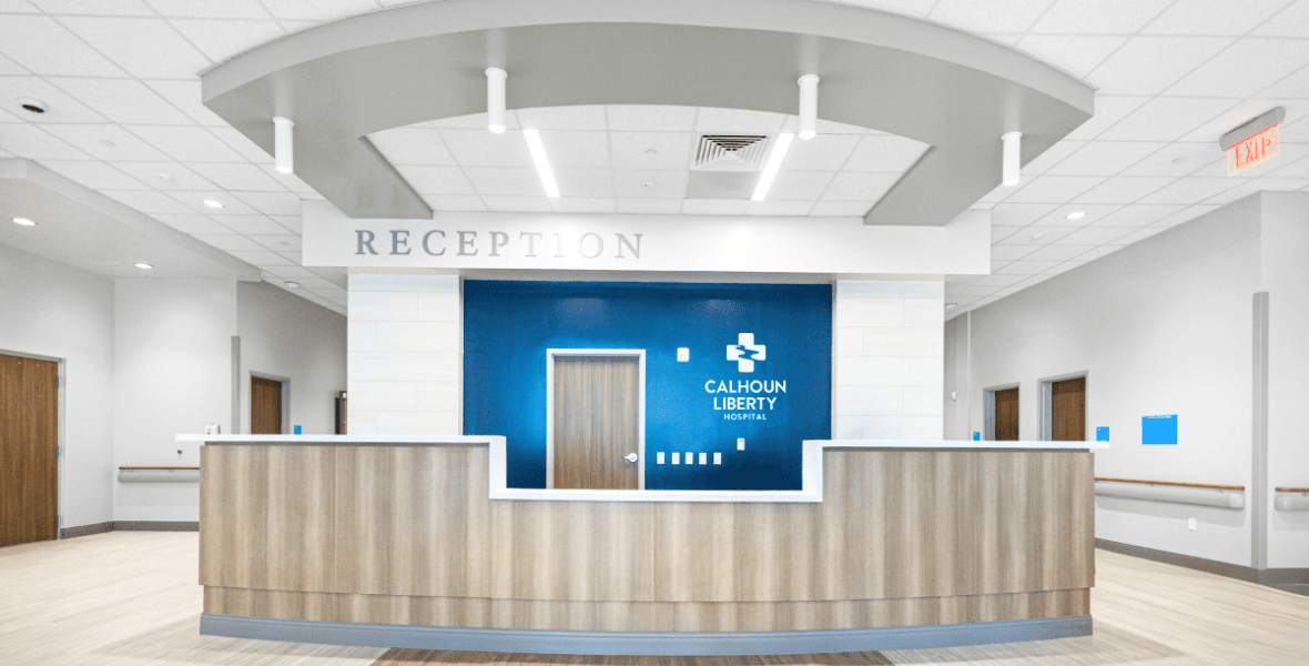 Modern wooden reception desk at Calhoun Liberty Hospital with a blue wall and white signage.