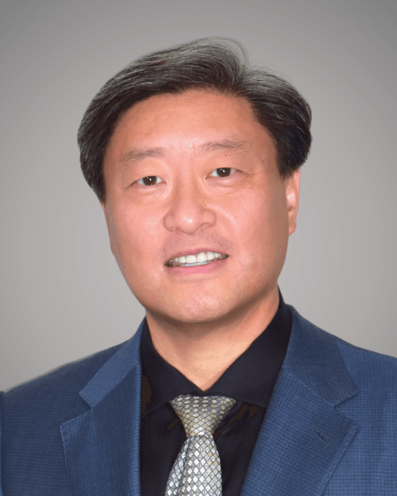 Smiling East Asian man with dark hair wearing a blue blazer and patterned tie.